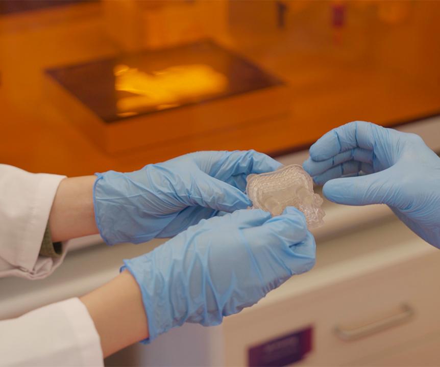 A close up of 2 researchers holding a clear plastic item produced in a UQ lab